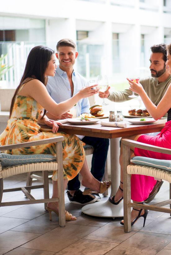 A group of four friends sits around a table enjoying a meal and drinks on an outdoor patio.