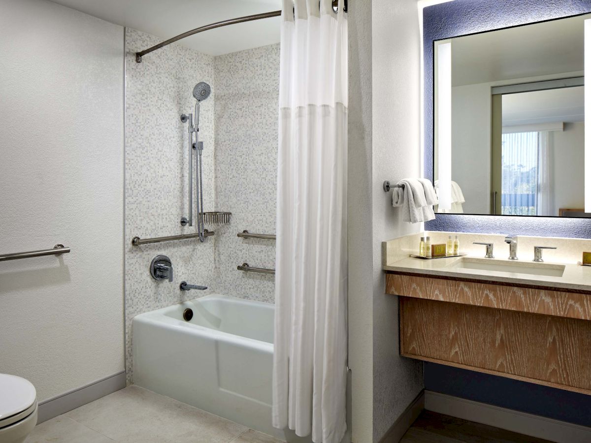 A bathroom with a bathtub/shower combo, white tiles, a shower curtain, a toilet, and a wooden vanity with a mirror and sink.