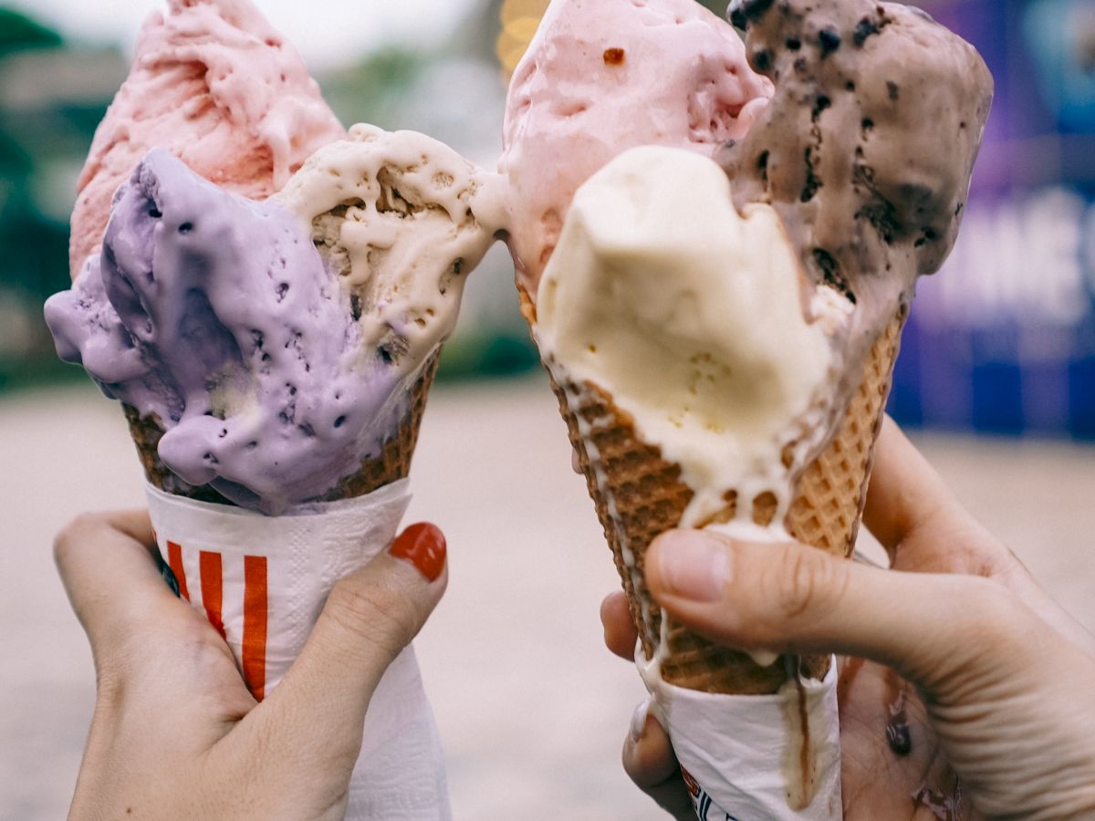 Two hands hold scoops of colorful ice cream cones, all melting slightly, ready to enjoy on a sunny day.
