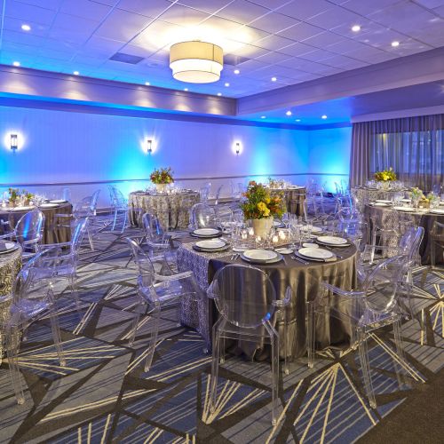 A stylish restaurant or event hall with round tables, beige chairs, and warm lighting. The room looks elegant and ready for a gathering.