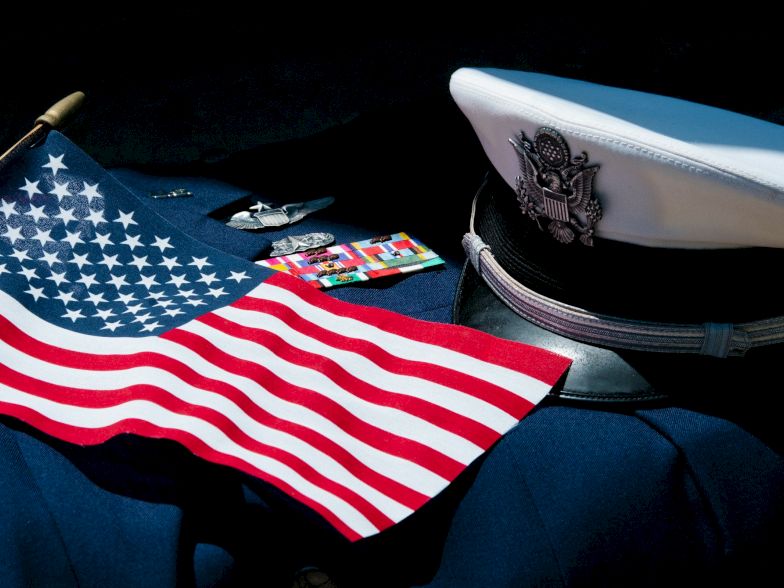 A U.S. flag and a captain&rsquo;s hat on a dark surface, with some small cards or items nearby, suggesting naval or patriotic theme. End sentence.