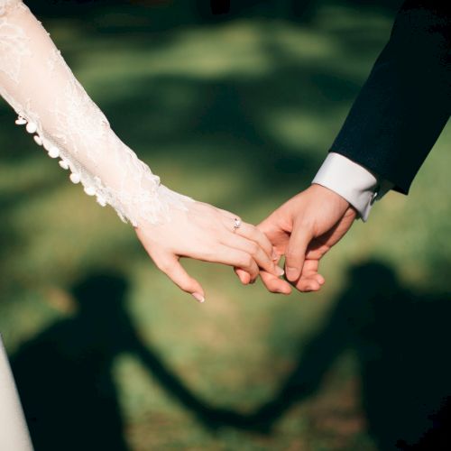 Two hands, a bride and groom, gently clasping love and unity on their wedding day, with soft shadows in the background.