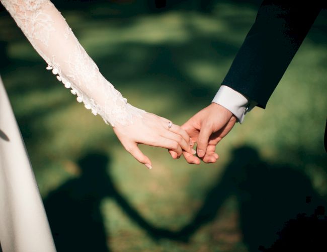 Two hands, a bride and groom, gently clasping love and unity on their wedding day, with soft shadows in the background.